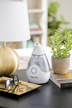Homedics TotalComfort Personal Ultrasonic Humidifier on a table with lamp, potted plant, and glassess