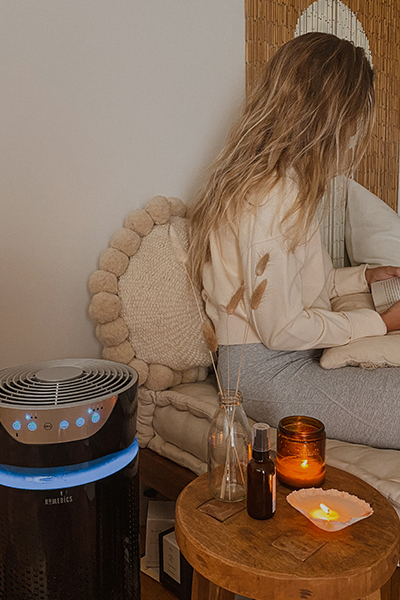 Woman sits in chair next to Homedics air purifier