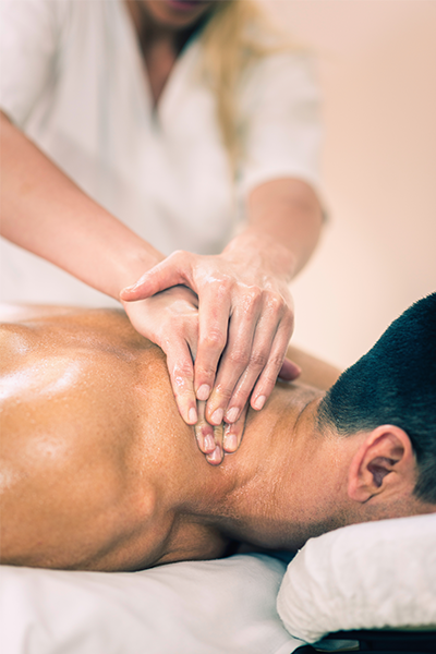 Muscular man lays on massage table and receives a neck massage from a professional masseuse. 