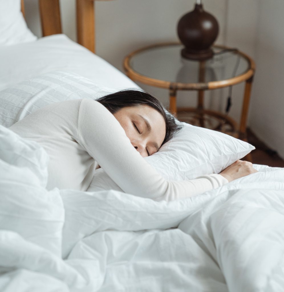 Woman in white shirt sleeps in a bed under a white comforter with white pillows