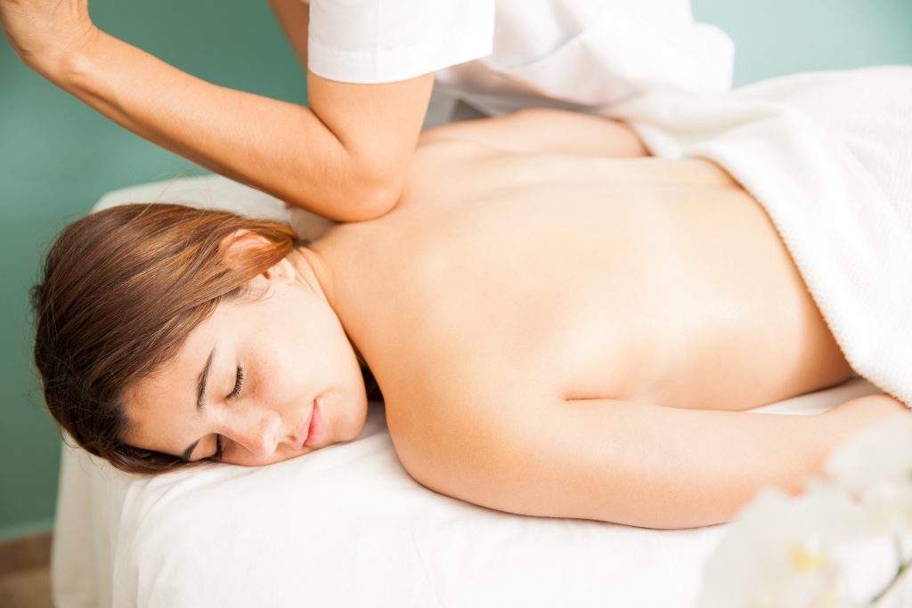 Woman laying on massage table receives shoulder massage from professional masseuse.