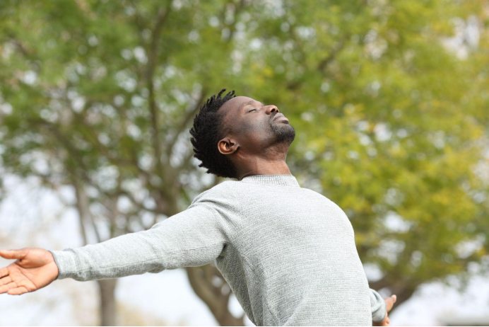 Man stands outside with arms extended to his sides and eyes closed as he takes in the sunshine