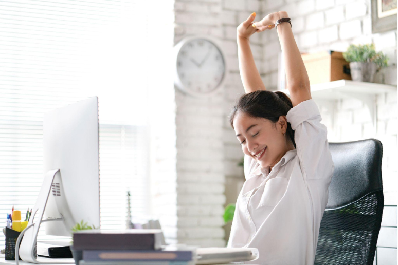Woman stretches her arms and medidtates at work desk in a brightly lit room