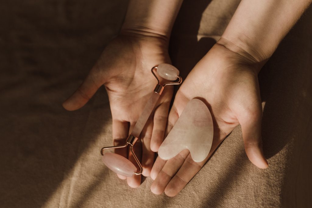 Hands hold up a jade roller and Gua sha tool in palm