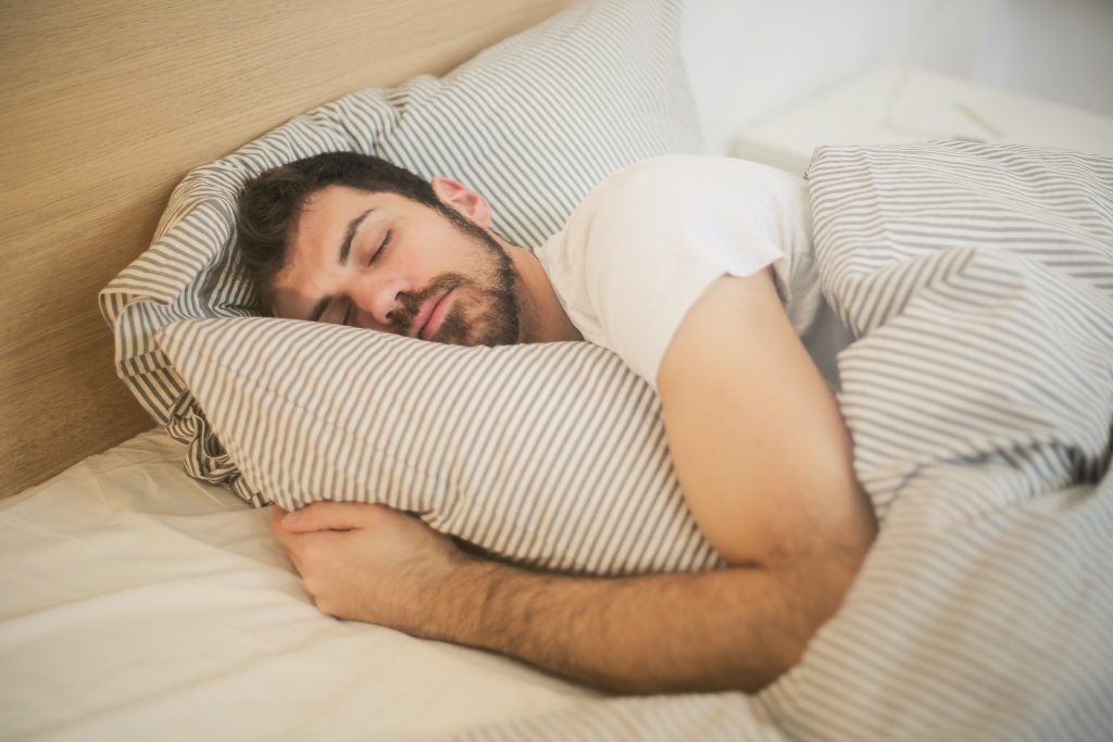Man in white t-shirt sleeps on pillow under the covers