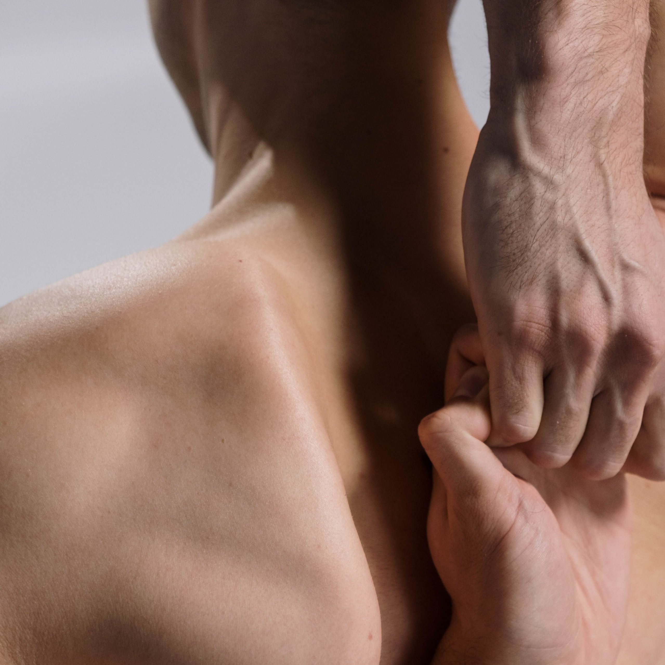 Shirtless man does shoulder stretches with hands linked behind back